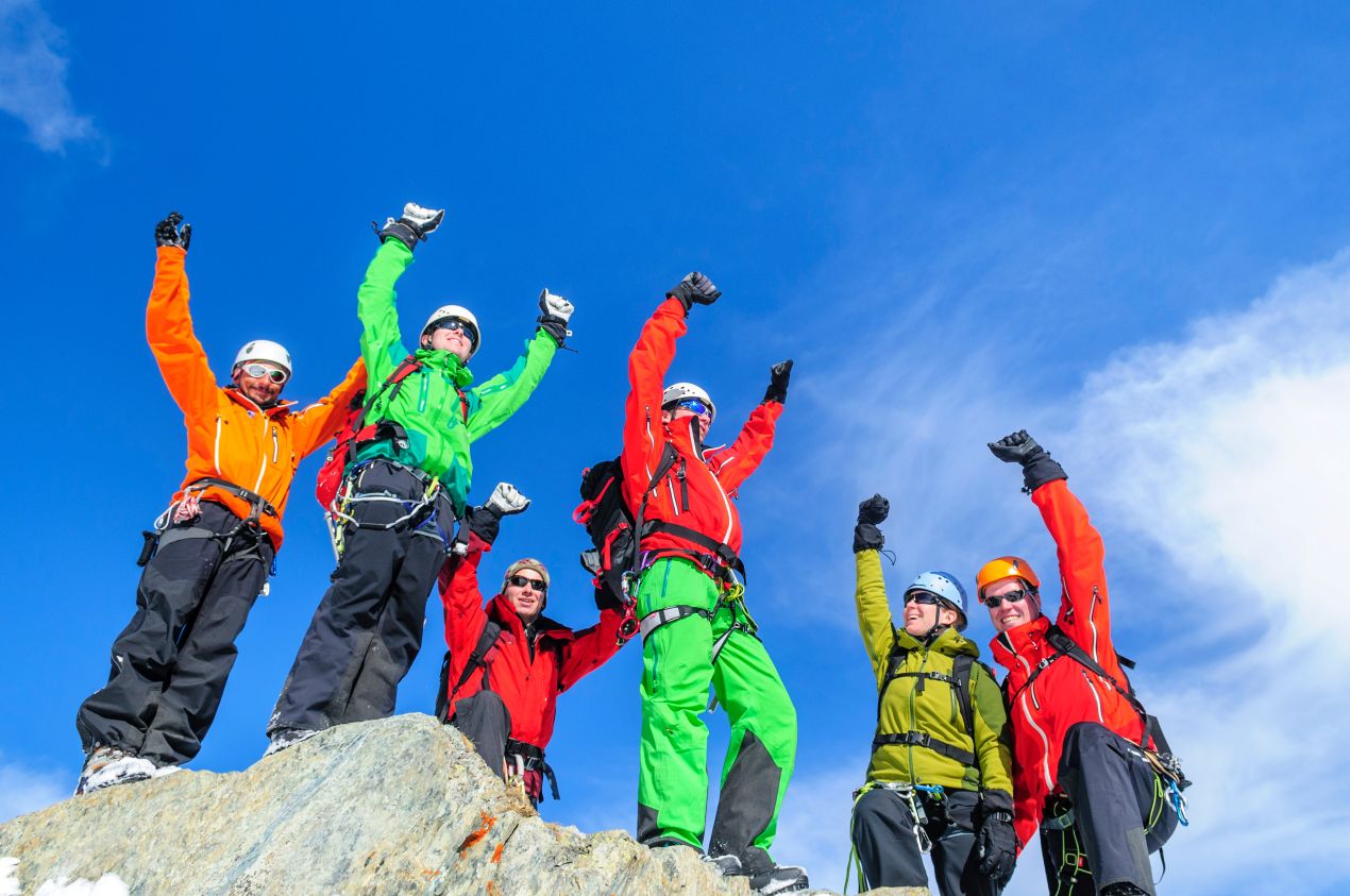 Eine Gruppe von Bergsteigern feiert auf einem Gipfel mit ausgestreckten Armen – der perfekte Abschluss nach der Besteigung Kilimandscharo.