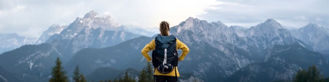 Eine Frau mit Rucksack genießt die Aussicht auf eine beeindruckende Bergkulisse, perfekt zur Vorbereitung auf die Besteigung Kilimandscharo.