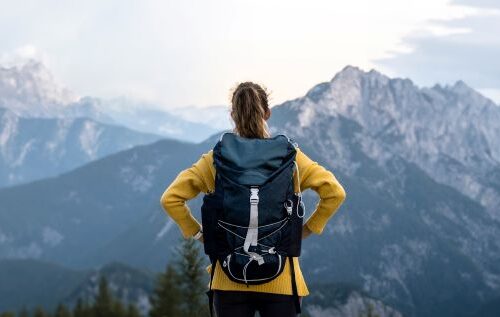 Eine Frau mit Rucksack genießt die Aussicht auf eine beeindruckende Bergkulisse, perfekt zur Vorbereitung auf die Besteigung Kilimandscharo.