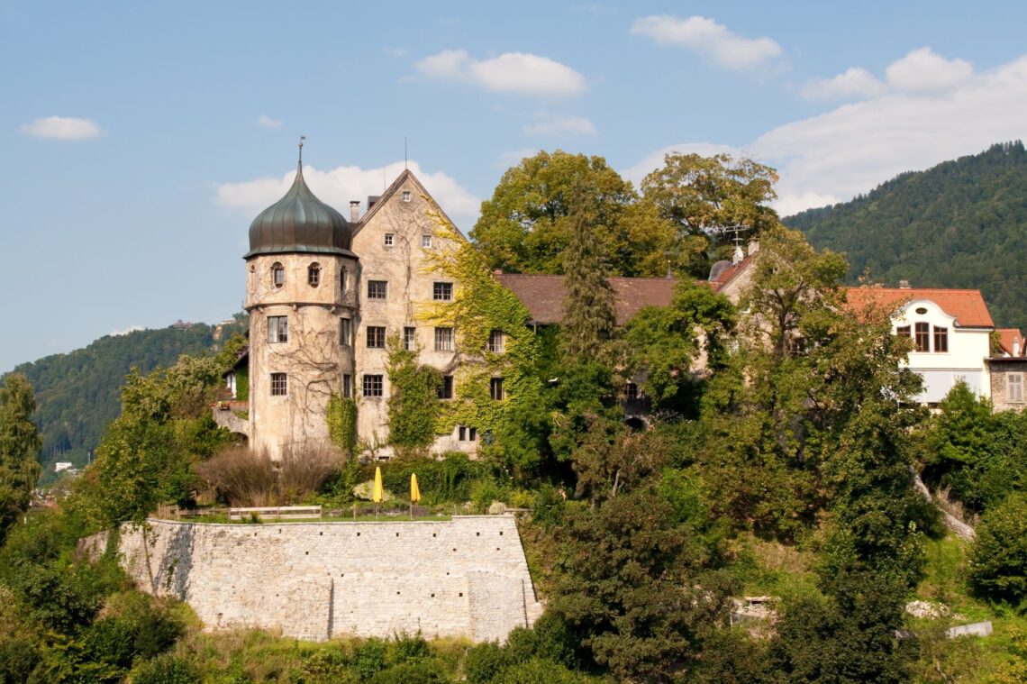 Historisches Schloss auf einem Hügel, umgeben von grüner Natur und mit Blick auf eine idyllische Landschaft