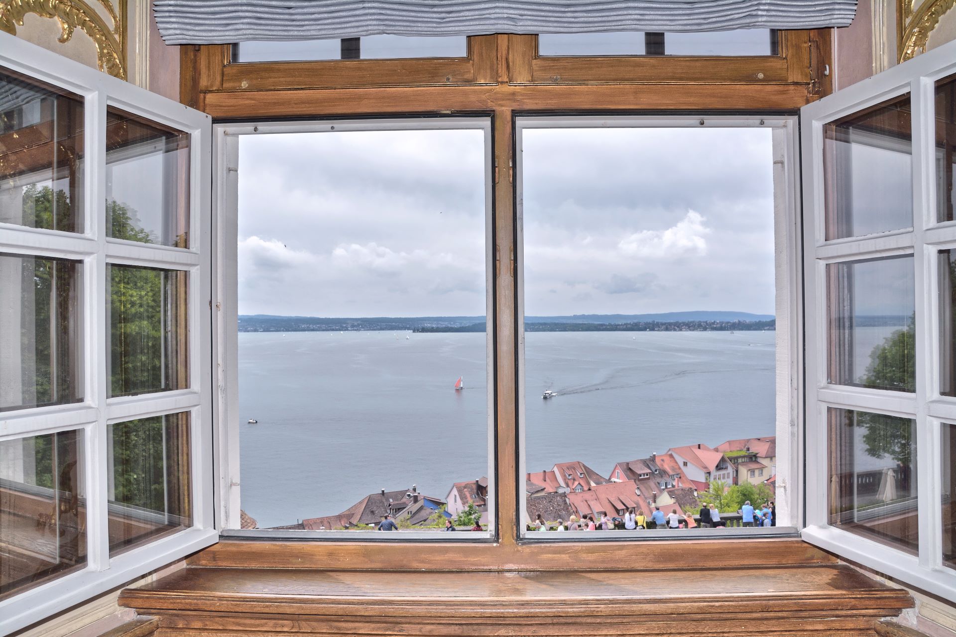 Offenes Fenster mit Blick auf den Bodensee, rote Dächer im Vordergrund und Segelboote auf dem Wasser.